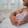 Woman applying body mosture in the bathroom at home